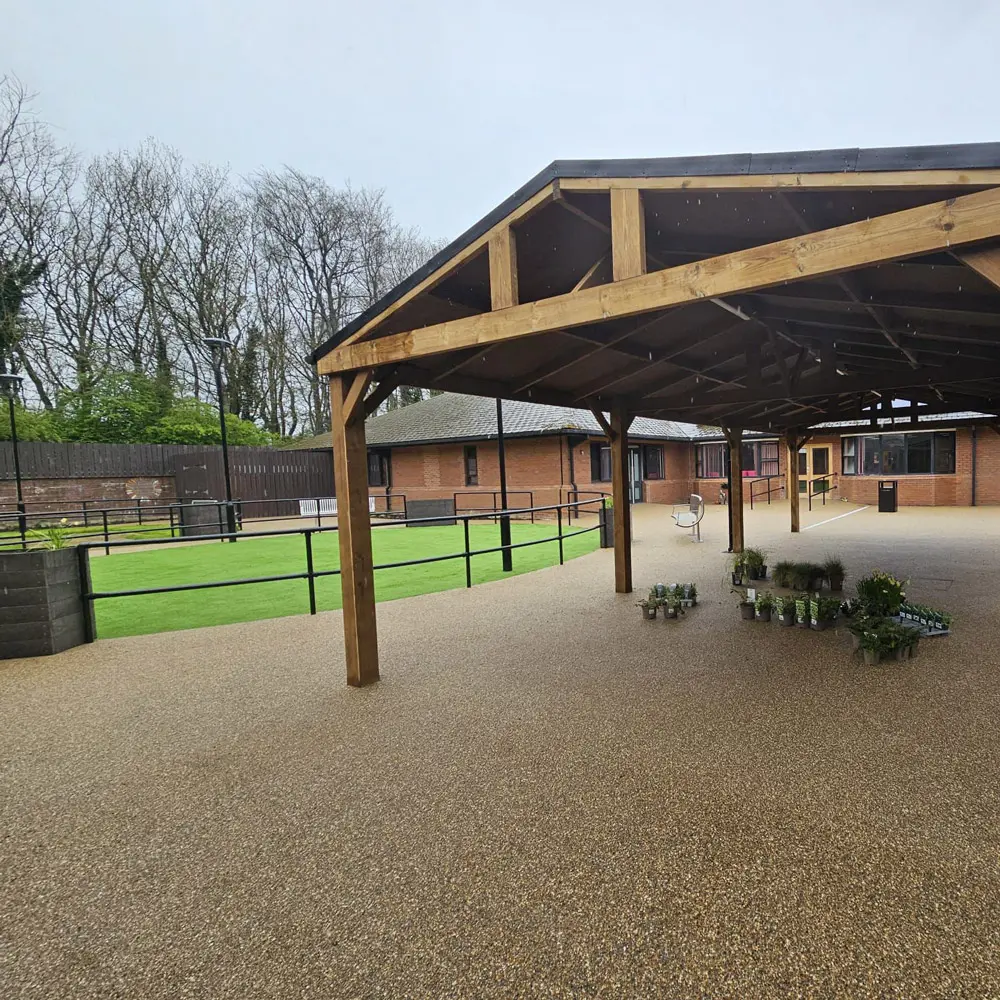 Commercial resin bound surface under timber canopy in care home courtyard with accessible pathways