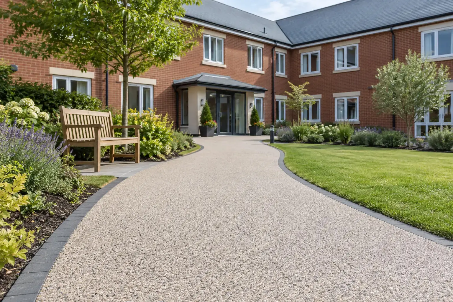 Illustrative resin bound pathway leading to a care home entrance, bordered by lawns and planting.