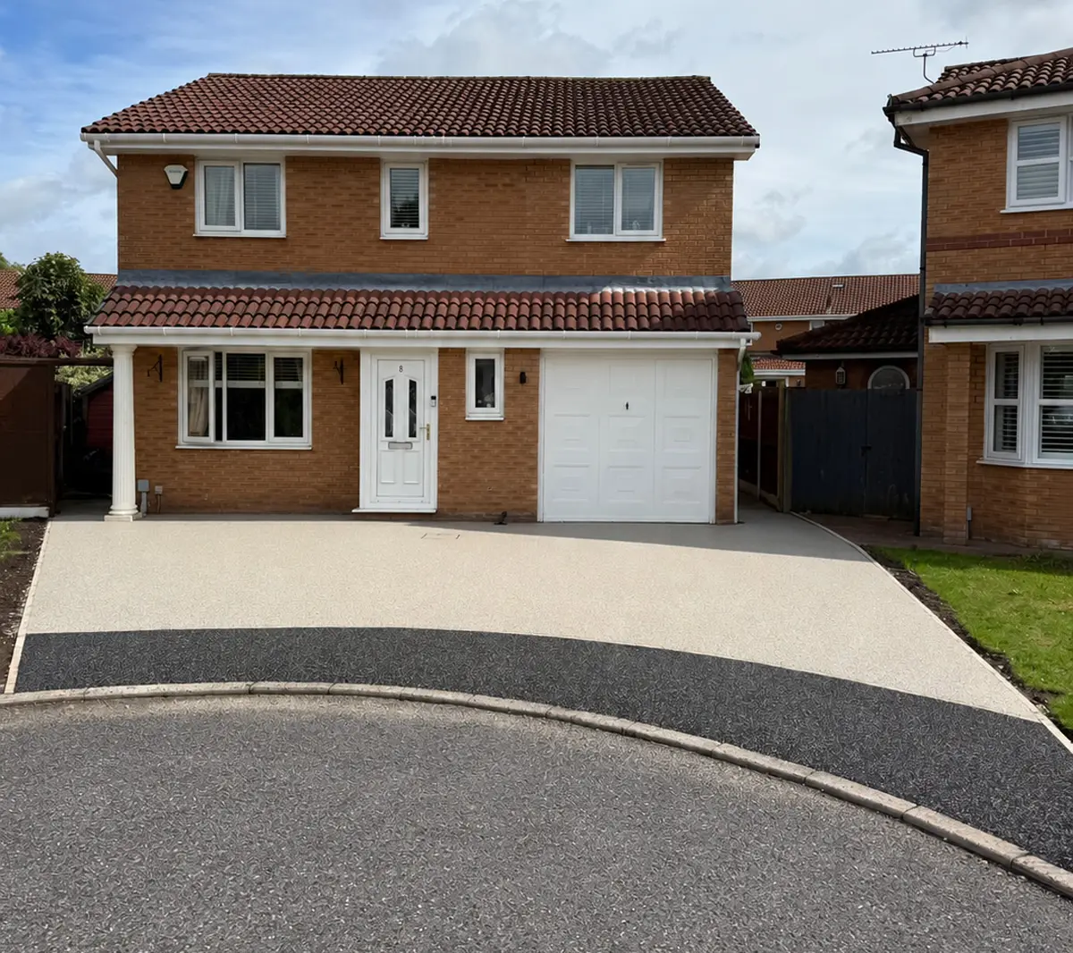 Light-coloured resin bound driveway with a curved dark grey border outside a detached brick house